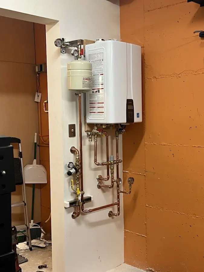 Plumbing technician inspecting water heater connections in Fenton